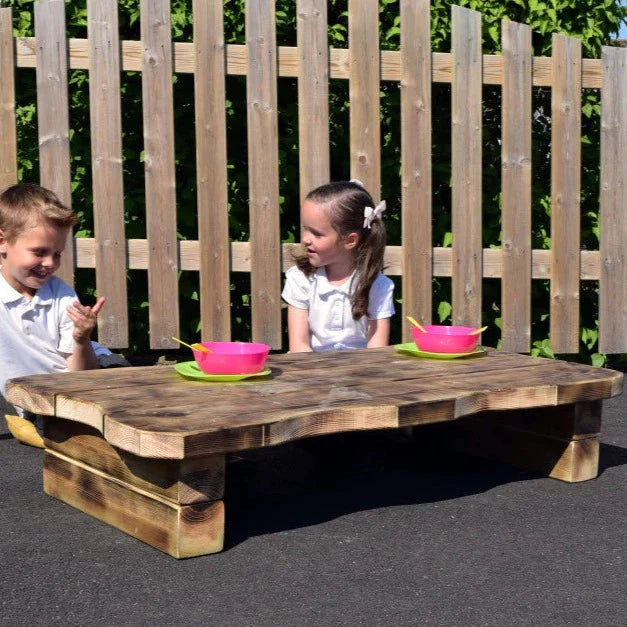 Outdoor Low Rustic Table, Enhance collaborative learning with our Outdoor Low Rustic Table! A versatile resource that can be used for both outdoor learning and eating lunch outdoors. Handmade in our Lincolnshire workshop, this rustic table was designed with adventure in mind. The idea is to create a comfy spot on the ground and gather around the table with friends for an adventurous lesson or picnic. Delivery 4-6 weeks, Delivered fully Assembled, FSC Pressure Treated Redwood Timber 10-year guarantee against