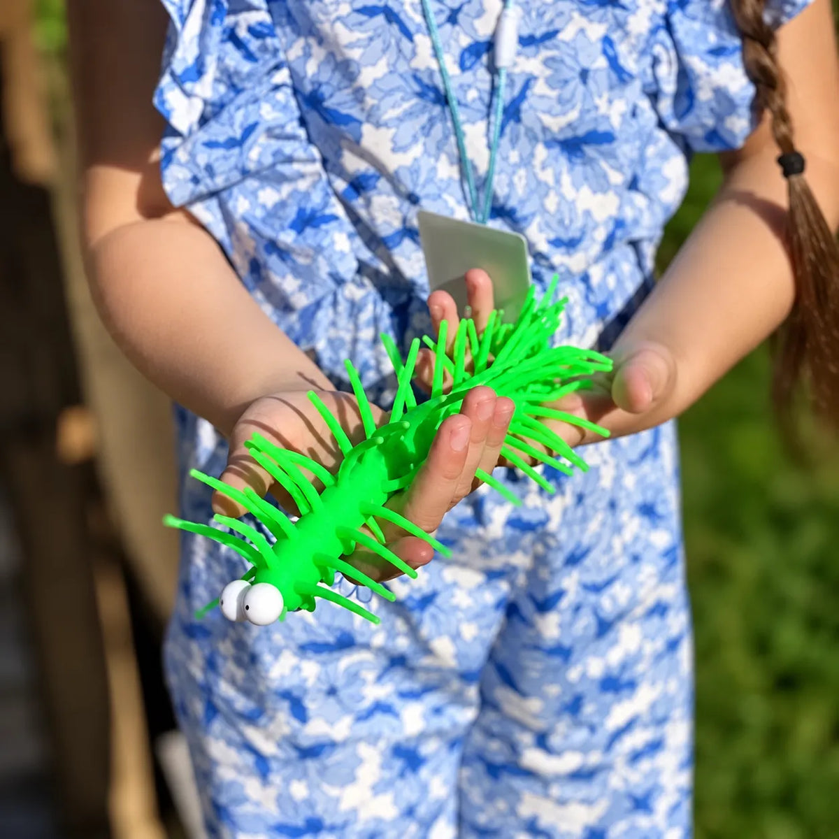 Green stretchy centipede toy held in a child's hands outdoors