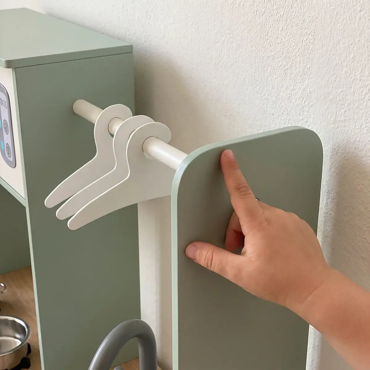 Three small hangers on the play kitchen rail