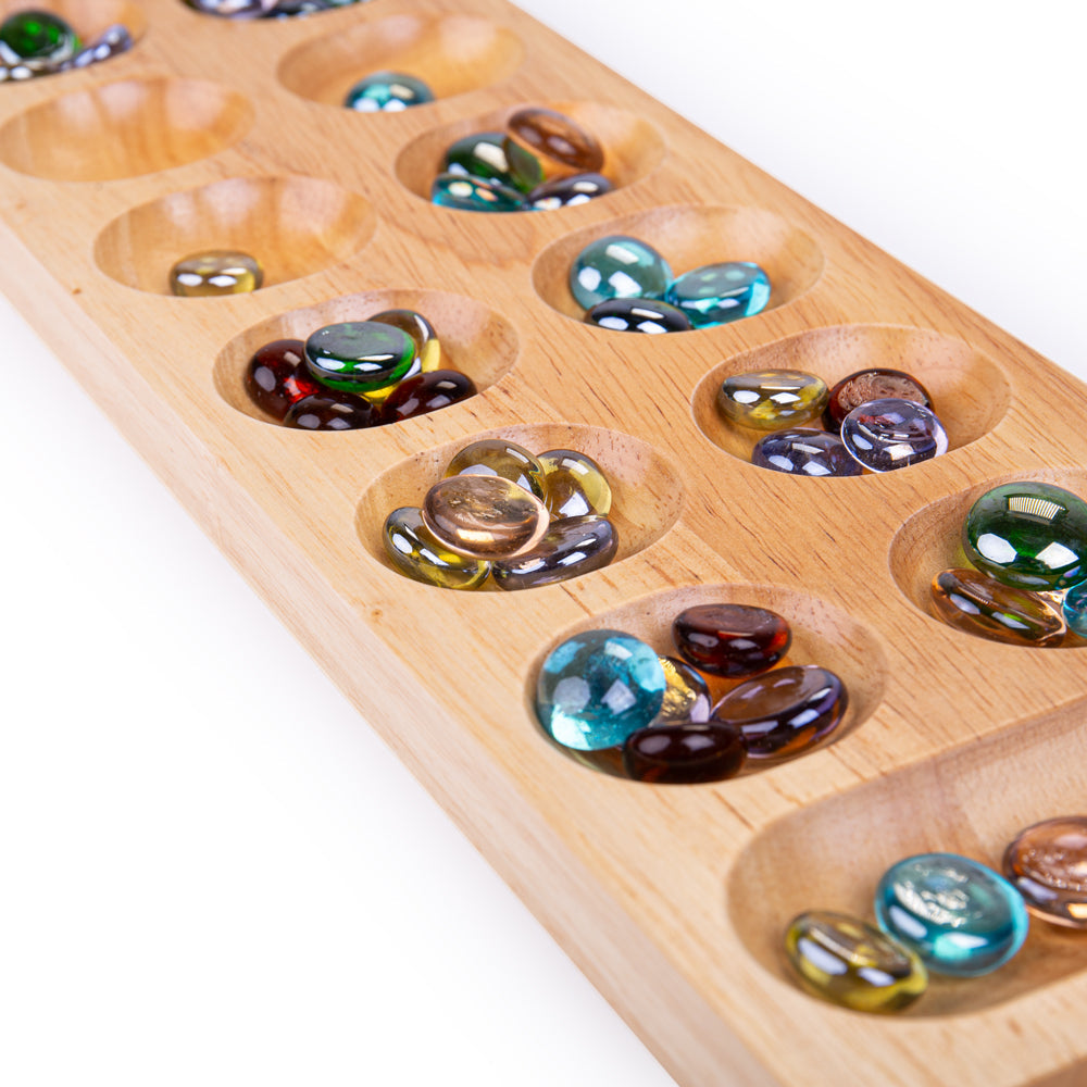 Mancala, Mancala is a two-player board game where the aim of the game is to collect more marbles than your opponent. This fun yet simple wooden board game comes with two rows of six holes and a long mancala at either end. Wondering how to play mancala? Begin by placing the four stones into each hole (don’t include the mandalas). To decide who’s going first by flipping a coin or doing rock-paper-scissors. During their turn, players must collect all of the marbles in a hole on their side of the board and drop