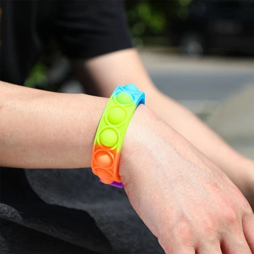 Rainbow Fidget Wristband, Introducing the Rainbow Fidget Wristband, the ultimate sensory tool that will keep you entertained and relaxed for hours on end. If you've ever found joy in popping bubble wrap, then this is the perfect gadget for you. This wristband is designed to divert a busy mind, providing a therapeutic experience that helps relieve stress and anxiety. Made from high-quality silicone, it features a series of mouse-shaped bubbles that can be easily pressed down to emit a satisfying popping soun